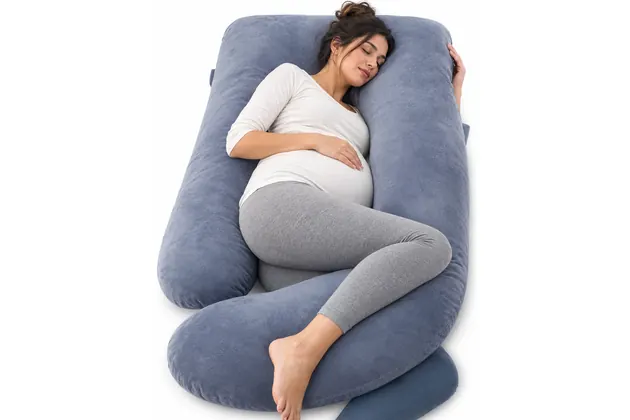 Pregnant woman sleeping on her side inside a slate-blue velvet U-shaped pregnancy pillow